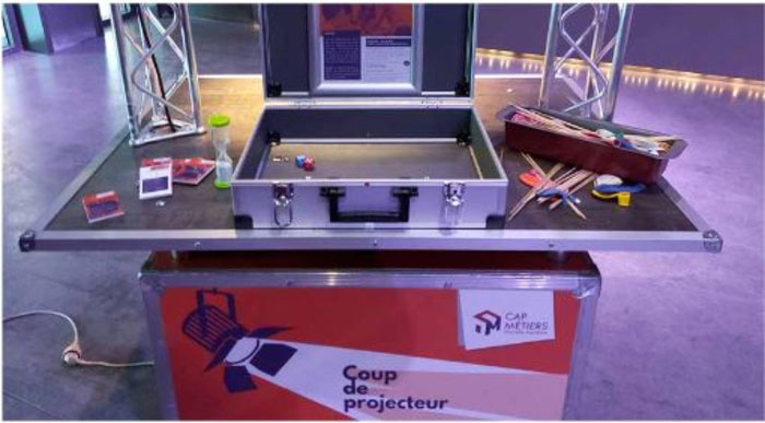 Mallette pédagogique ouverte sur une table, accompagnée d’outils ludiques, dans le cadre de l’exposition "Coup de projecteur" de Cap Métiers Nouvelle-Aquitaine.