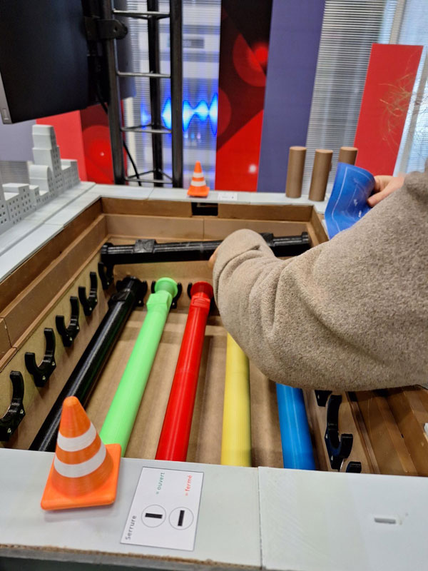 Un participant manipule une maquette illustrant un réseau de canalisations multicolores, utilisé pour simuler les réseaux souterrains dans les travaux publics.