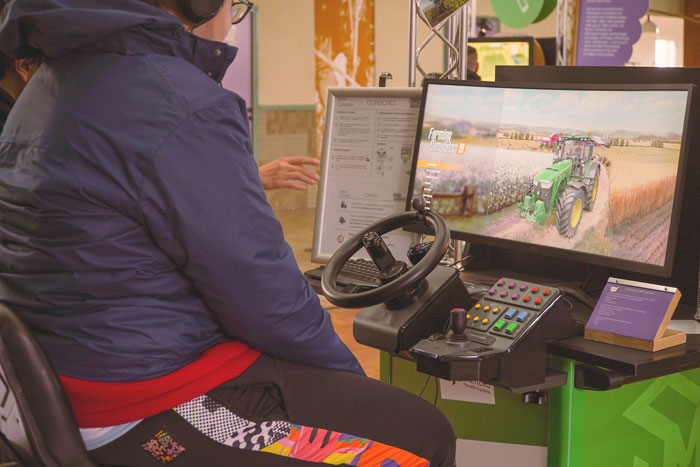 Un jeune utilise un simulateur de conduite avec volant et écran pour découvrir les gestes professionnels liés à la conduite de tracteurs dans le secteur agricole et viticole.