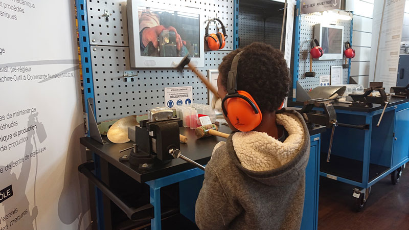 Un enfant équipé d’un casque antibruit participe à un atelier de rivetage lors de l’exposition « Décollage immédiat » sur les métiers de l’aéronautique et du spatial.
